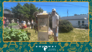 Empower N L volunteer Travis mans the popcorn machine while members enjoy the carnival in the background. The Empower N L logo is centered at the bottom.