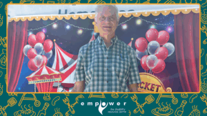 An Empower N L member poses in front of the carnival wall. The Empower N L logo is centered at the bottom.