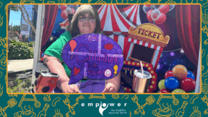 Empower N L member Terri poses for a photo in front of a carnival backdrop. The Empower N L logo is centered at the bottom.