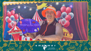 Empower N L member Kim poses in front of the carnival wall. The Empower N L logo is centered at the bottom.