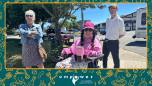 Three members of Empower N L, one using a power wheelchair, smile in the sunshine with trees behind. The Empower N L logo is centered at the bottom.